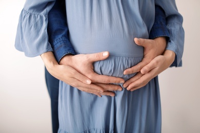 Photo of Young pregnant couple on light background, closeup of hands