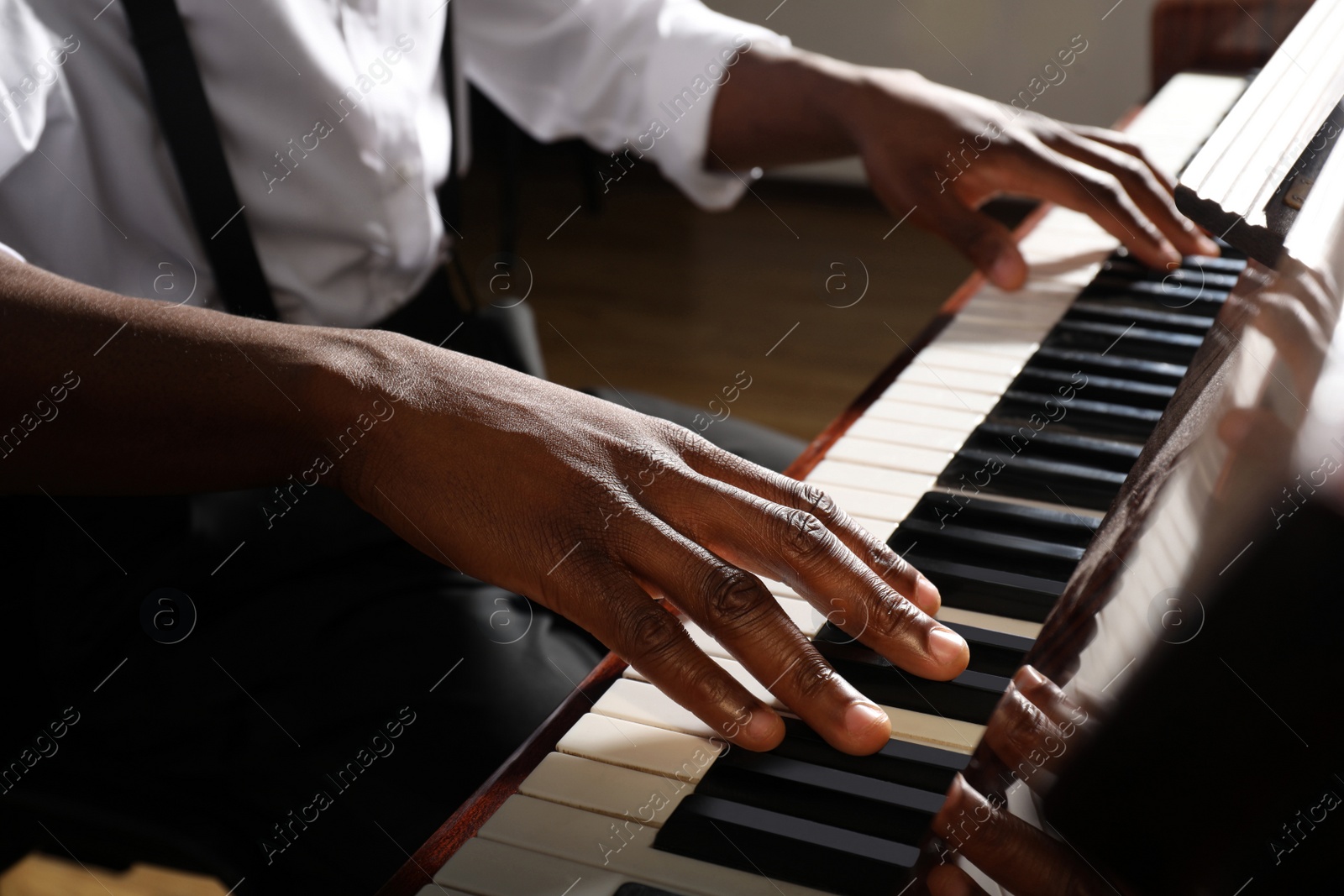 Photo of African-American man playing piano indoors, closeup. Talented musician