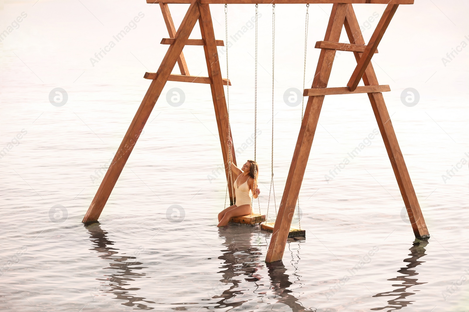 Photo of Young woman enjoying sunrise on swing over water