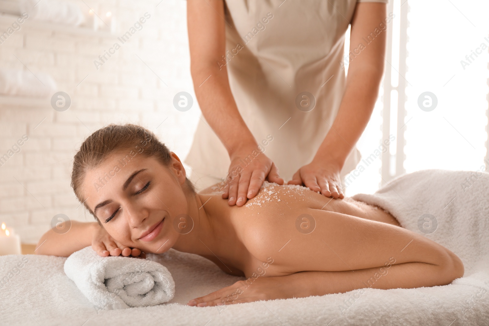 Photo of Young woman having body scrubbing procedure with sea salt in spa salon