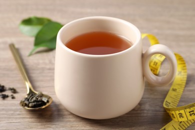 Photo of Cup of herbal diet tea and measuring tape on wooden table, closeup. Weight loss concept