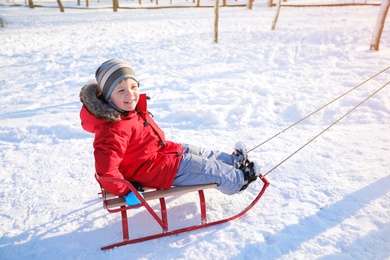 Photo of Cute little boy enjoying sleigh ride in snowy park