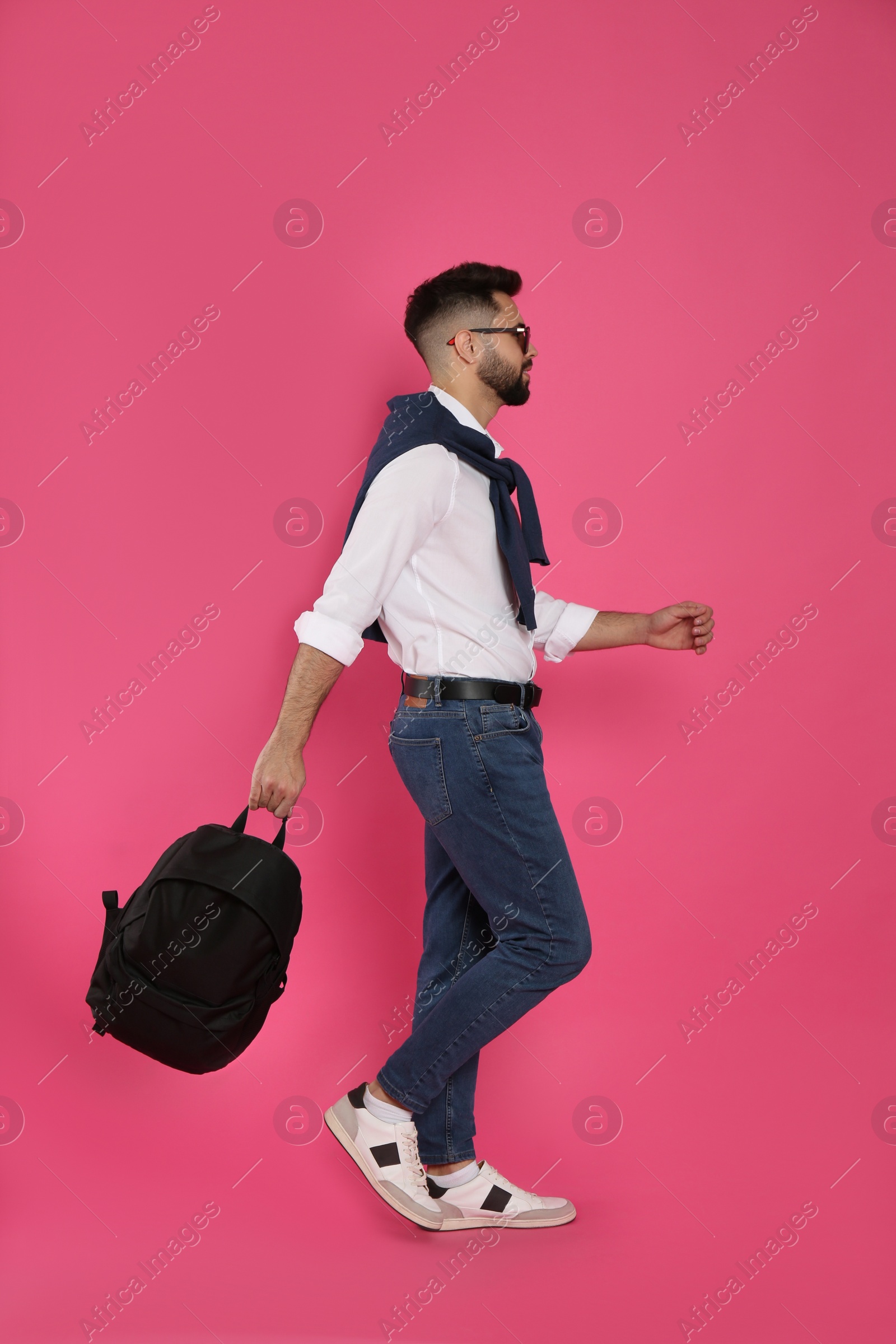 Photo of Young man with stylish backpack walking on pink background