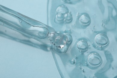Photo of Dripping cosmetic serum from pipette onto light blue background, macro view