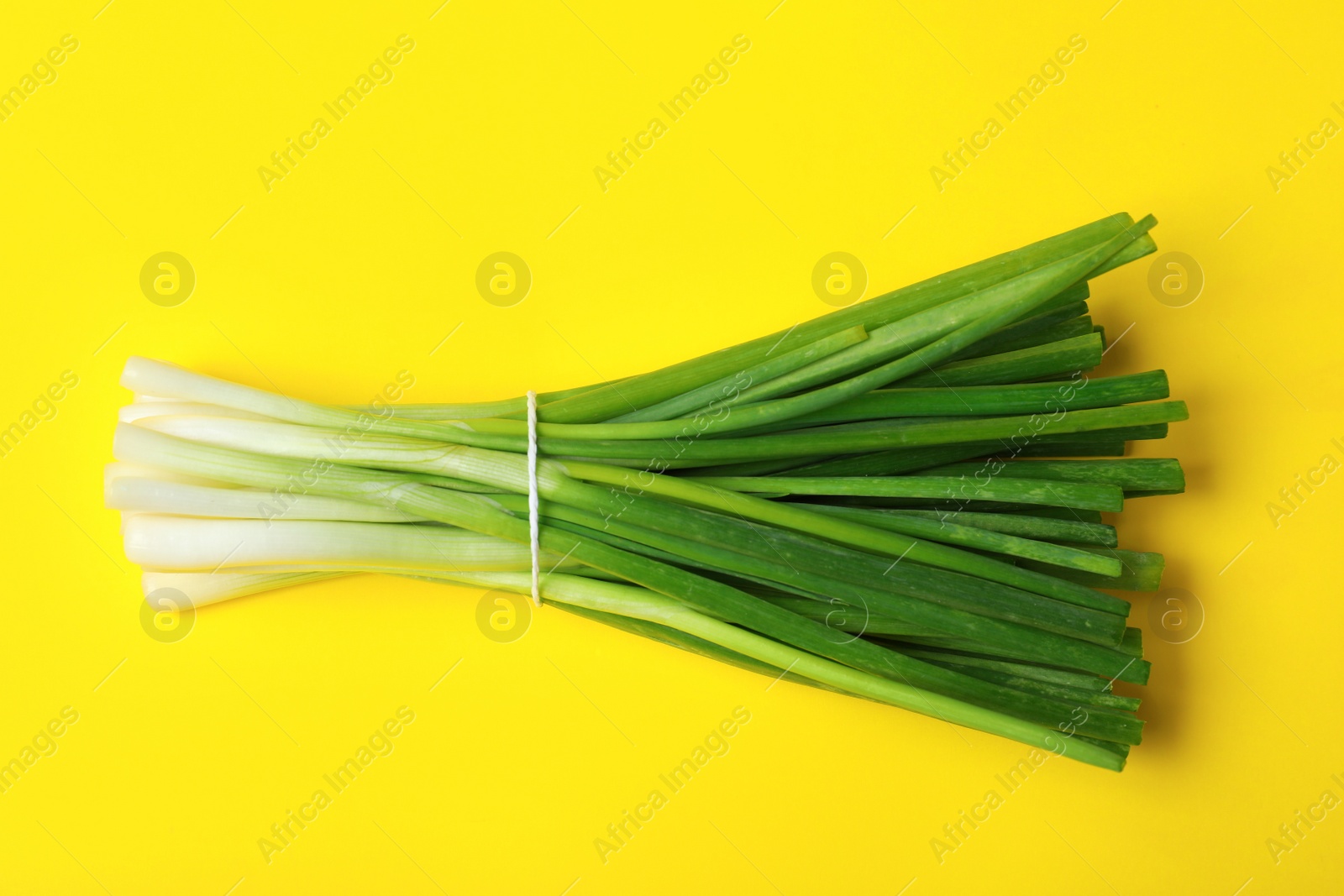 Photo of Bunch of fresh green onion on yellow background