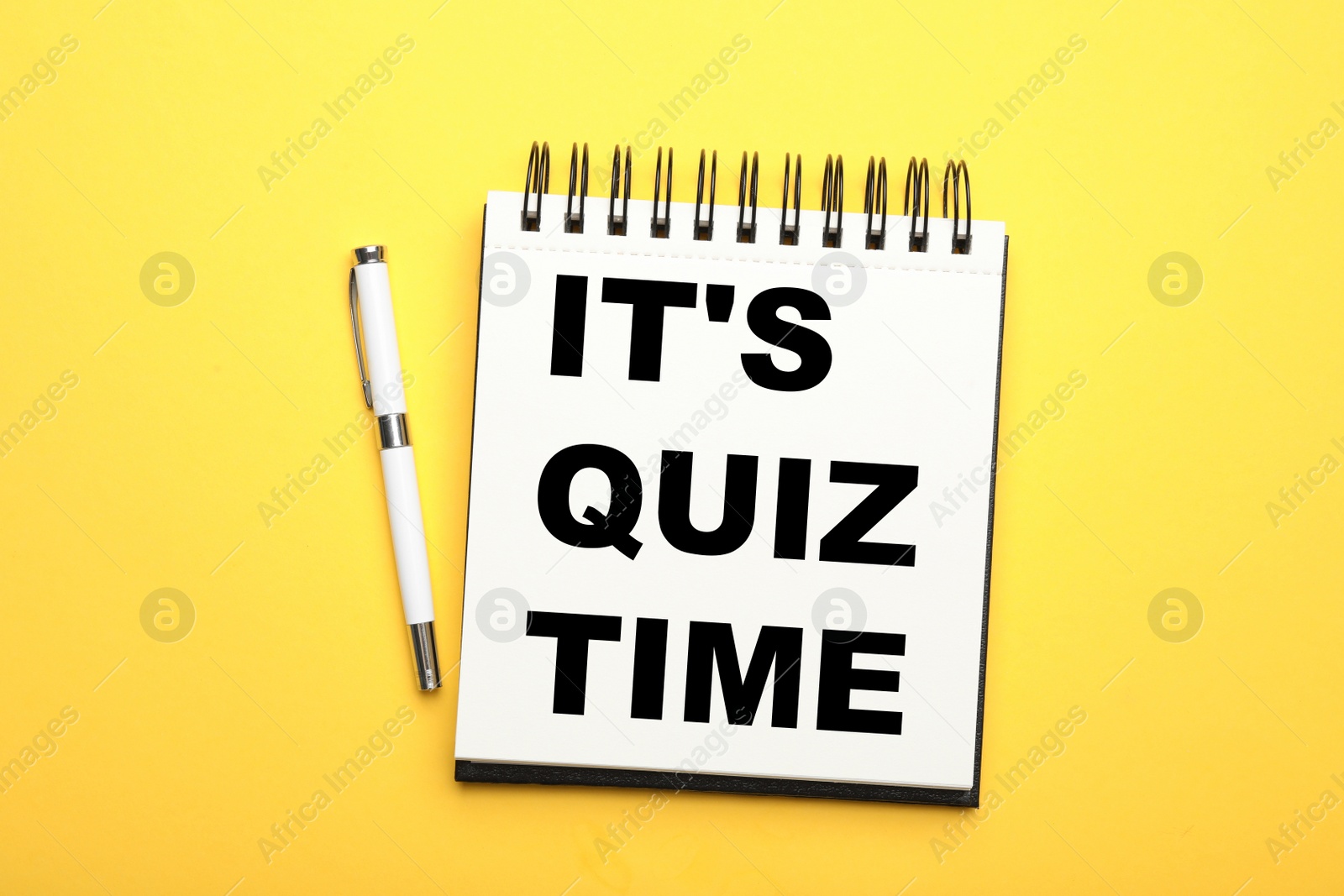 Image of Phrase It's quiz time written in notebook and pen on yellow background, flat lay