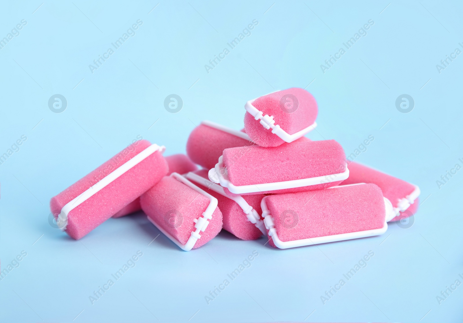 Photo of Many pink hair curlers on light blue background