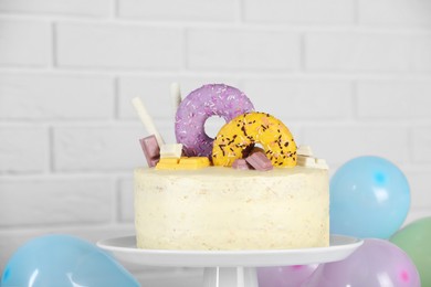 Delicious cake decorated with sweets and balloons against white brick wall