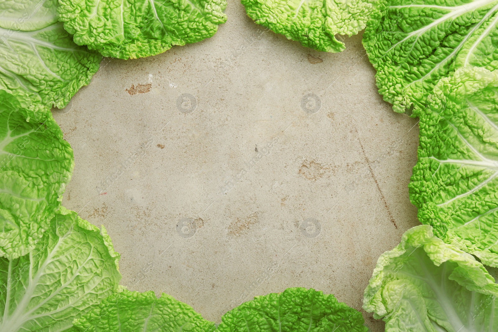 Photo of Frame of fresh Chinese cabbage leaves on gray textured table, top view. Space for text