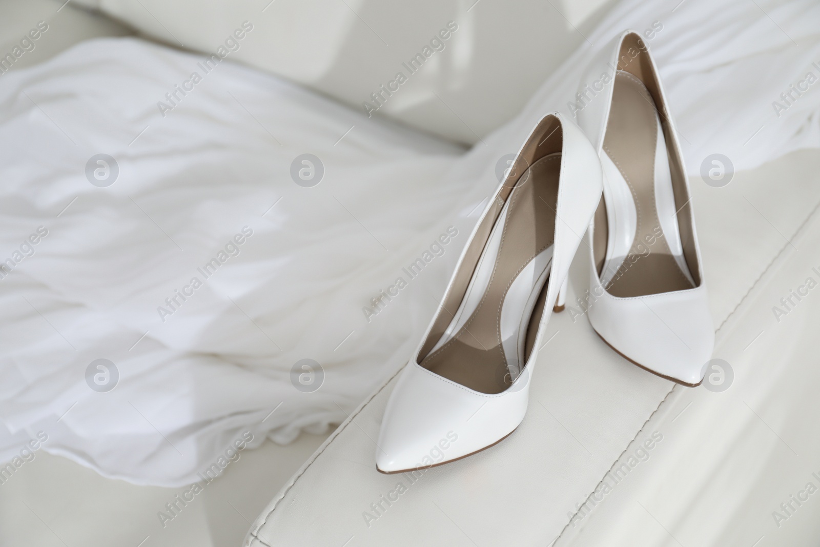 Photo of Classic white wedding shoes on sofa indoors