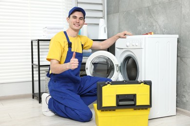 Photo of Smiling plumber showing thumb up near washing machine in bathroom