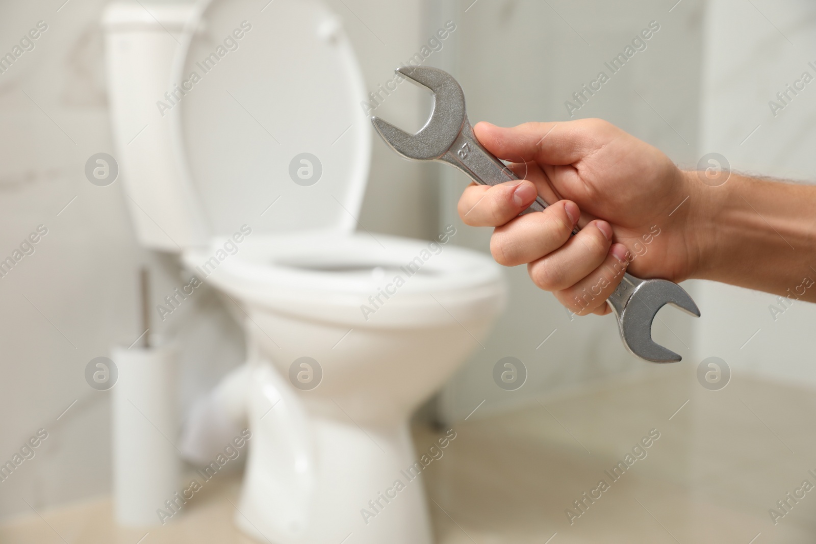 Photo of Professional plumber holding wrench near toilet bowl in bathroom, closeup