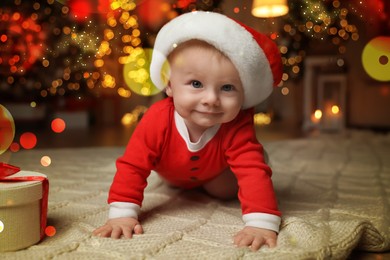 Cute baby in Santa hat with Christmas gift on floor at home