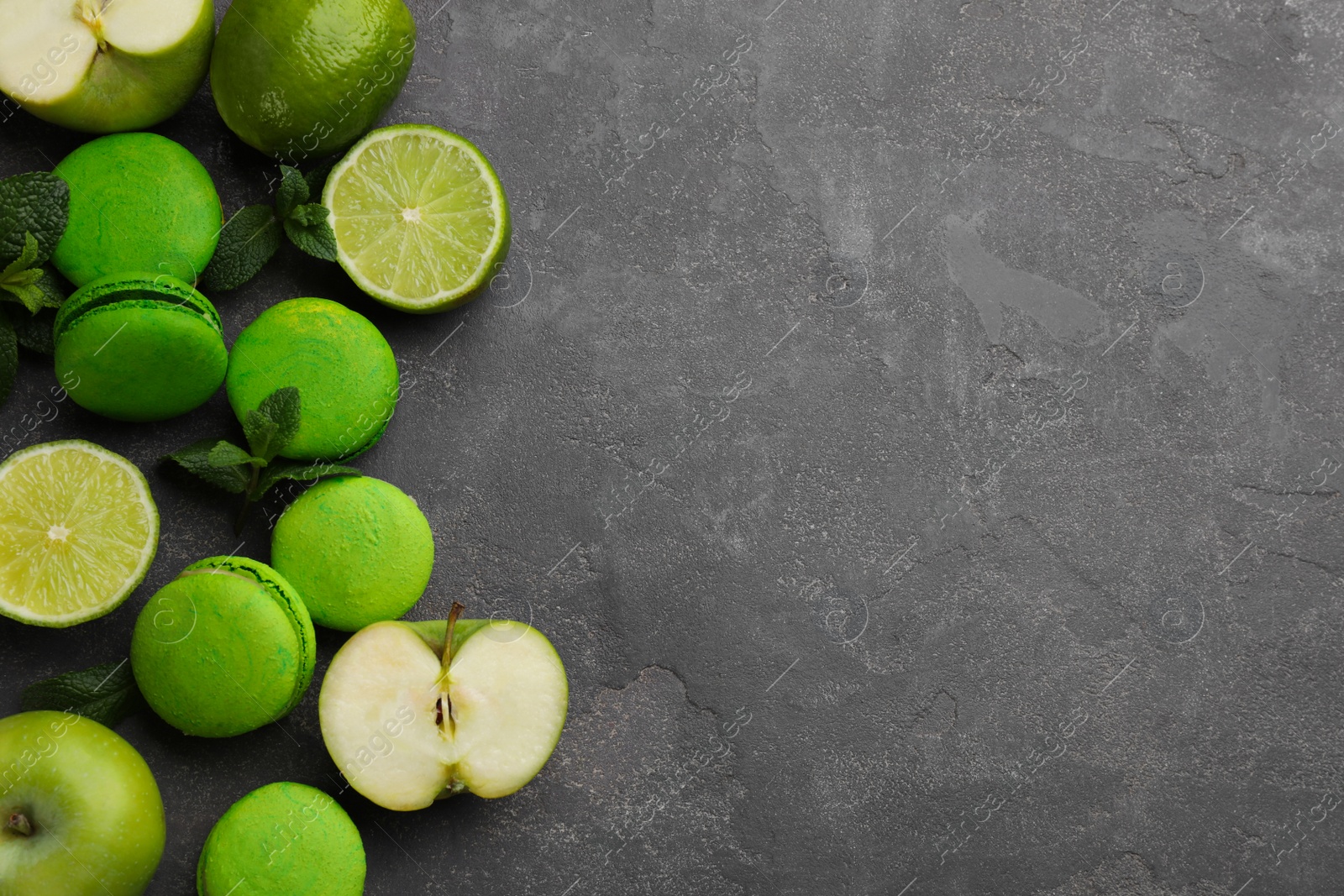 Photo of Delicious green macarons, mint and fresh fruits on grey table, flat lay. Space for text