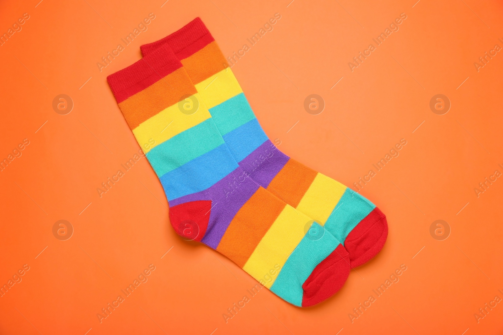 Photo of Rainbow socks on orange background, flat lay. LGBT pride