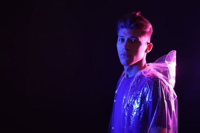 Young man wearing clear coat on dark background in neon lights. Space for text