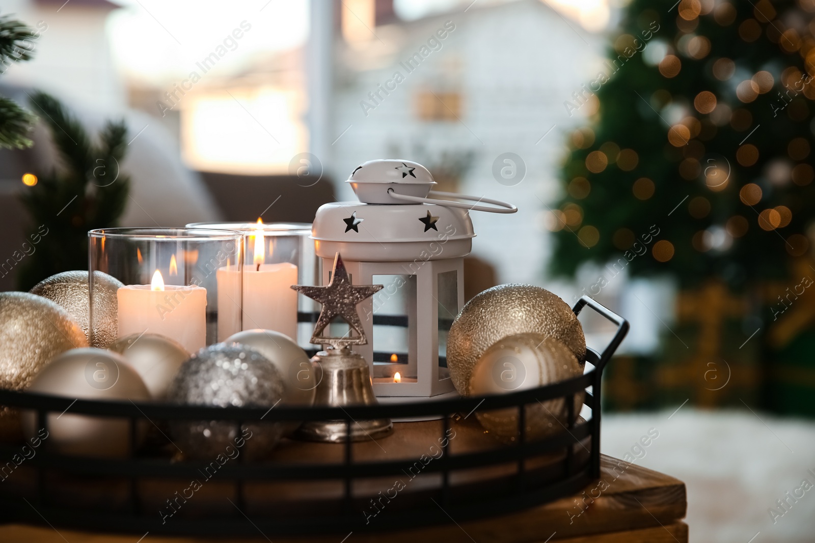 Photo of Burning candles, lantern and Christmas balls on wooden table indoors, closeup