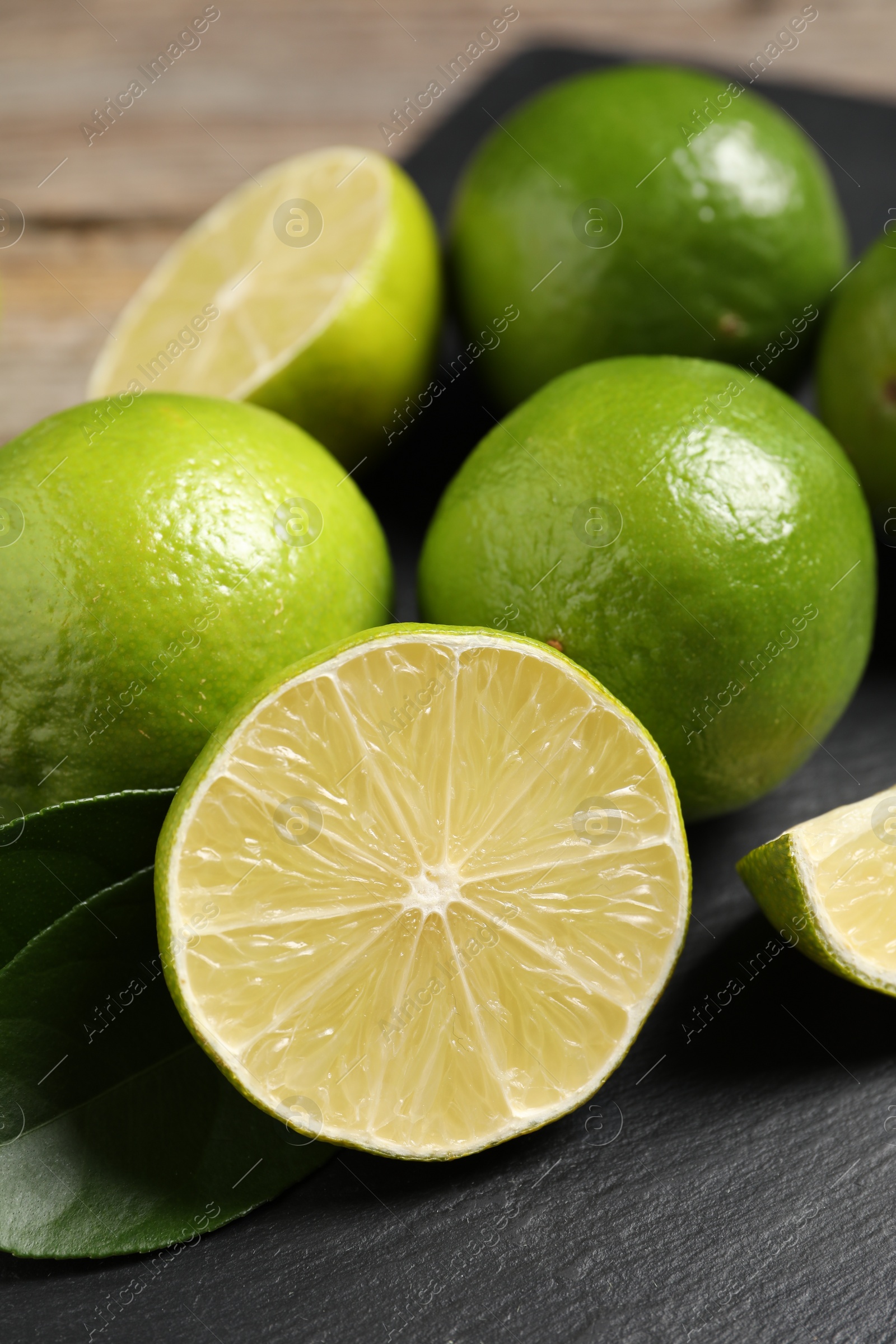 Photo of Fresh limes and green leaves on black board, closeup