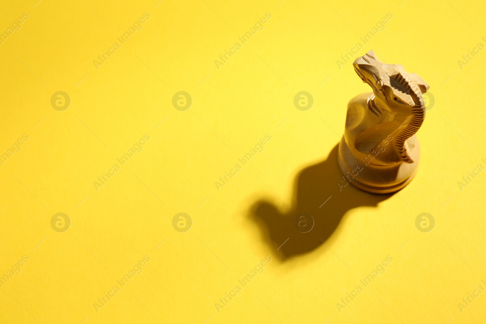 Photo of White wooden chess knight on yellow background, above view. Space for text