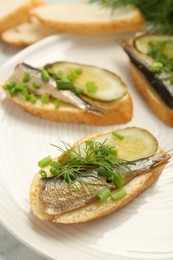 Photo of Delicious sandwiches with sprats, pickled cucumber, green onion and dill on plate, closeup