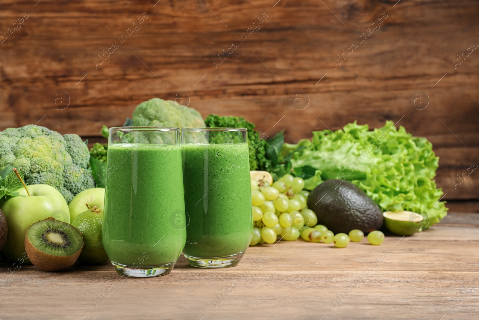 Photo of Glasses of fresh green smoothie and ingredients on wooden table, space for text