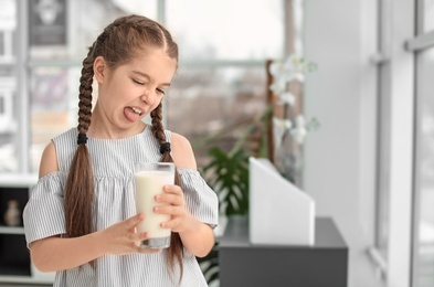 Little girl with dairy allergy holding glass of milk indoors