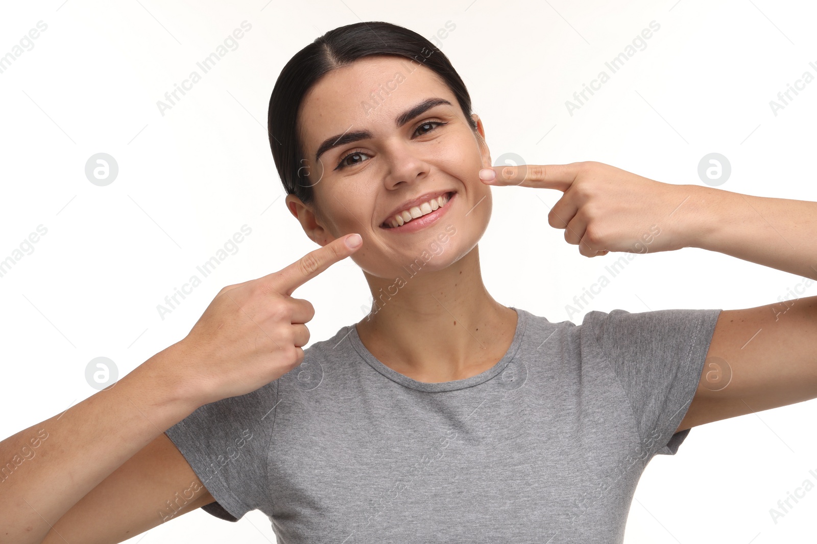 Photo of Young woman pointing at her clean teeth and smiling on white background