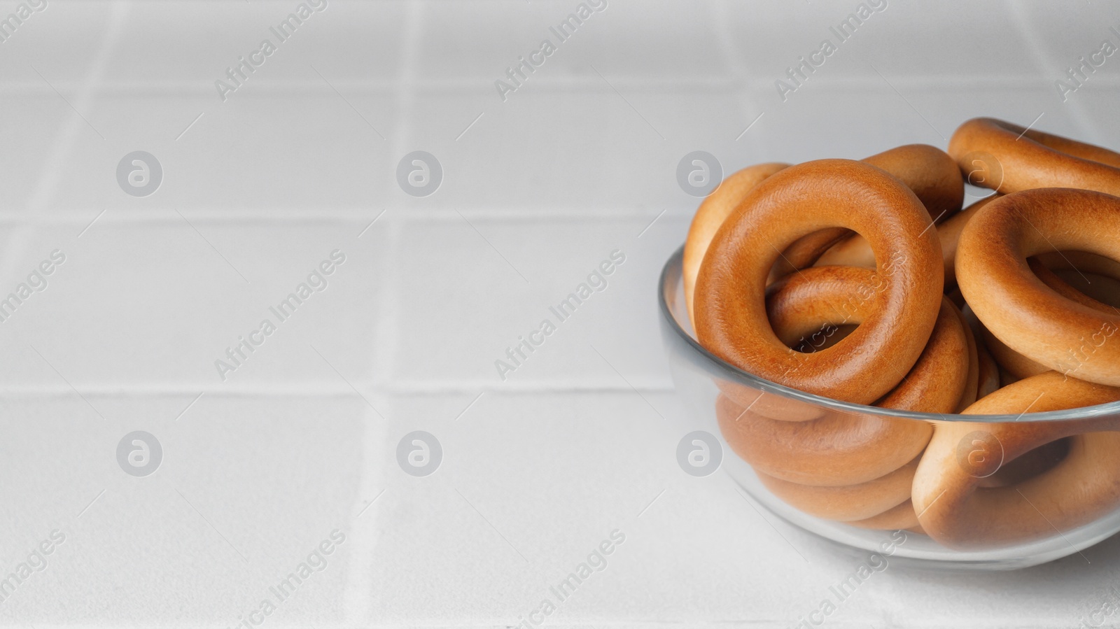 Photo of Bowl of tasty dry bagels (sushki) on white tiled table, space for text