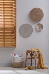 Wooden stool with dress and wicker basket near light  grey wall indoors. Interior accessories