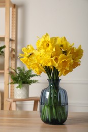 Beautiful daffodils in vase on wooden table indoors