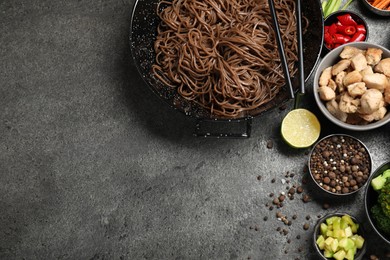 Photo of Wok with noodles, chicken and other products on grey table, flat lay. Space for text