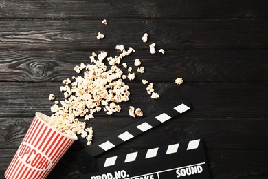 Tasty popcorn and clapperboard on wooden background, top view. Cinema snack