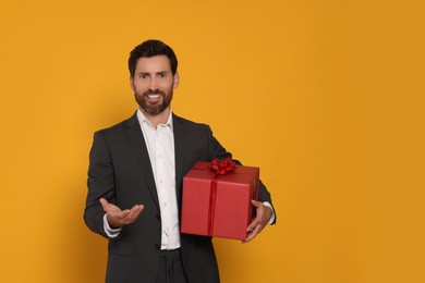 Photo of Handsome man holding gift box on yellow background, space for text