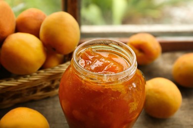 Photo of Jar of delicious jam and fresh ripe apricots on wooden table indoors, closeup. Fruit preserve