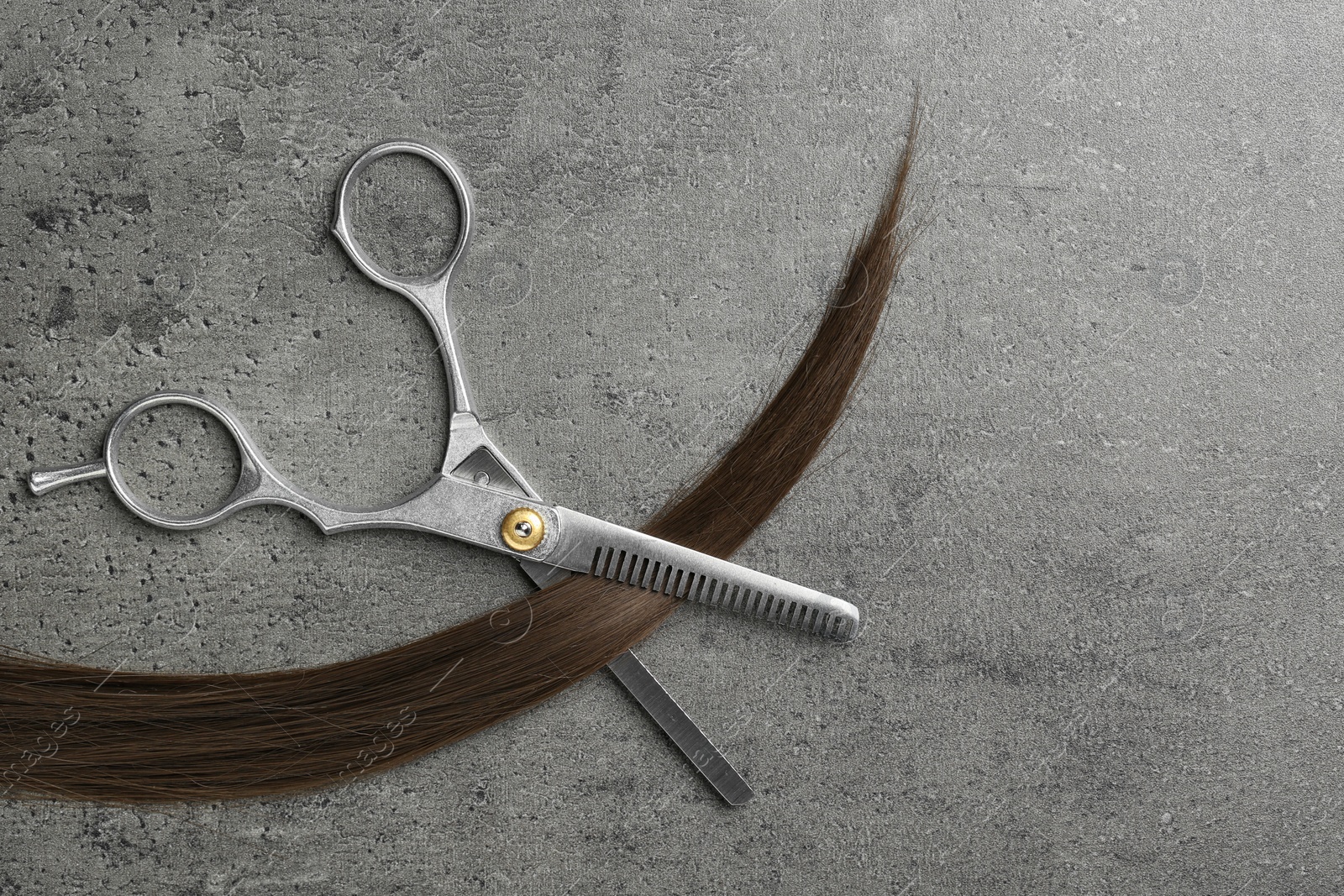 Photo of Flat lay composition with strand of brown hair and thinning scissors on grey background. Hairdresser service