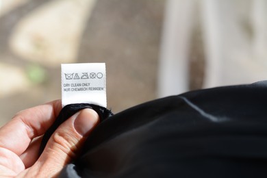 Photo of Woman holding clothing label on black garment, closeup