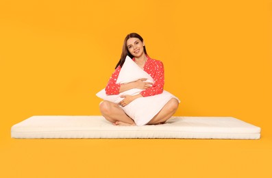 Young woman on soft mattress holding pillow against orange background