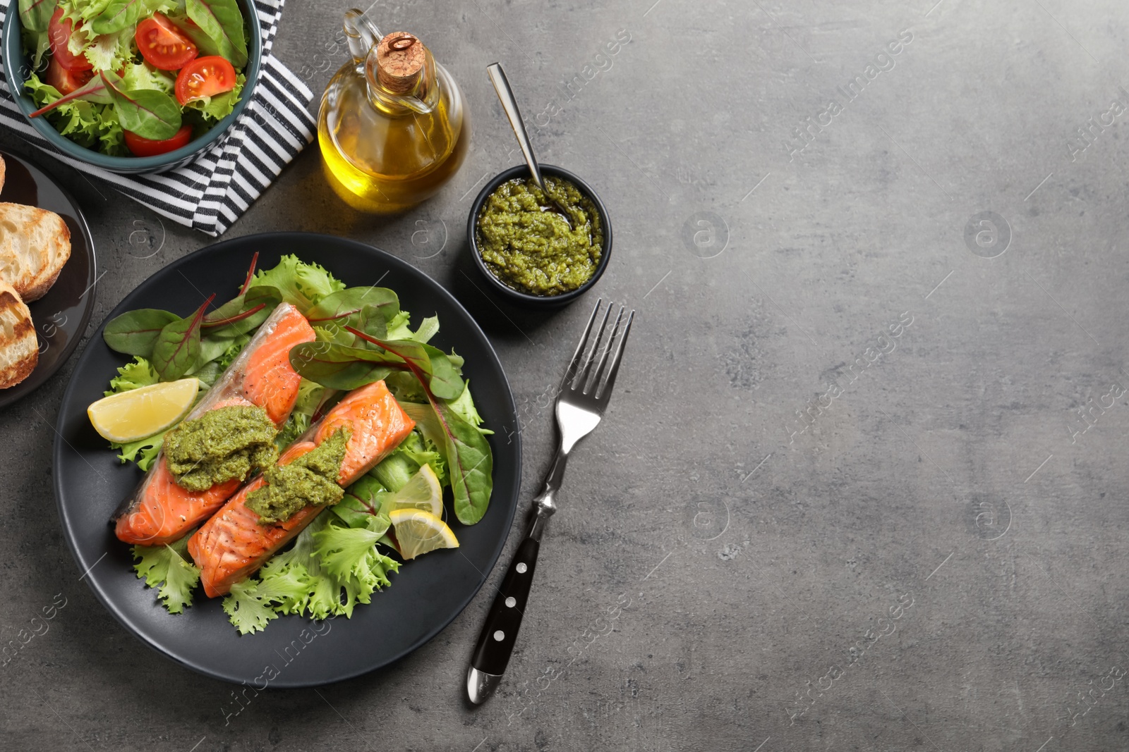 Photo of Tasty cooked salmon with pesto sauce served on dark grey table, flat lay. Space for text