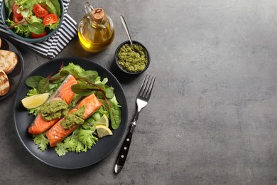 Photo of Tasty cooked salmon with pesto sauce served on dark grey table, flat lay. Space for text