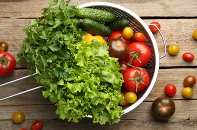 Photo of Fresh vegetables in colander on wooden table, flat lay