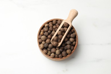 Photo of Dry allspice berries (Jamaica pepper) in bowl and scoop on white marble table, top view