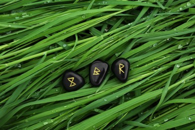 Black rune stones on green grass with water drops outdoors, top view