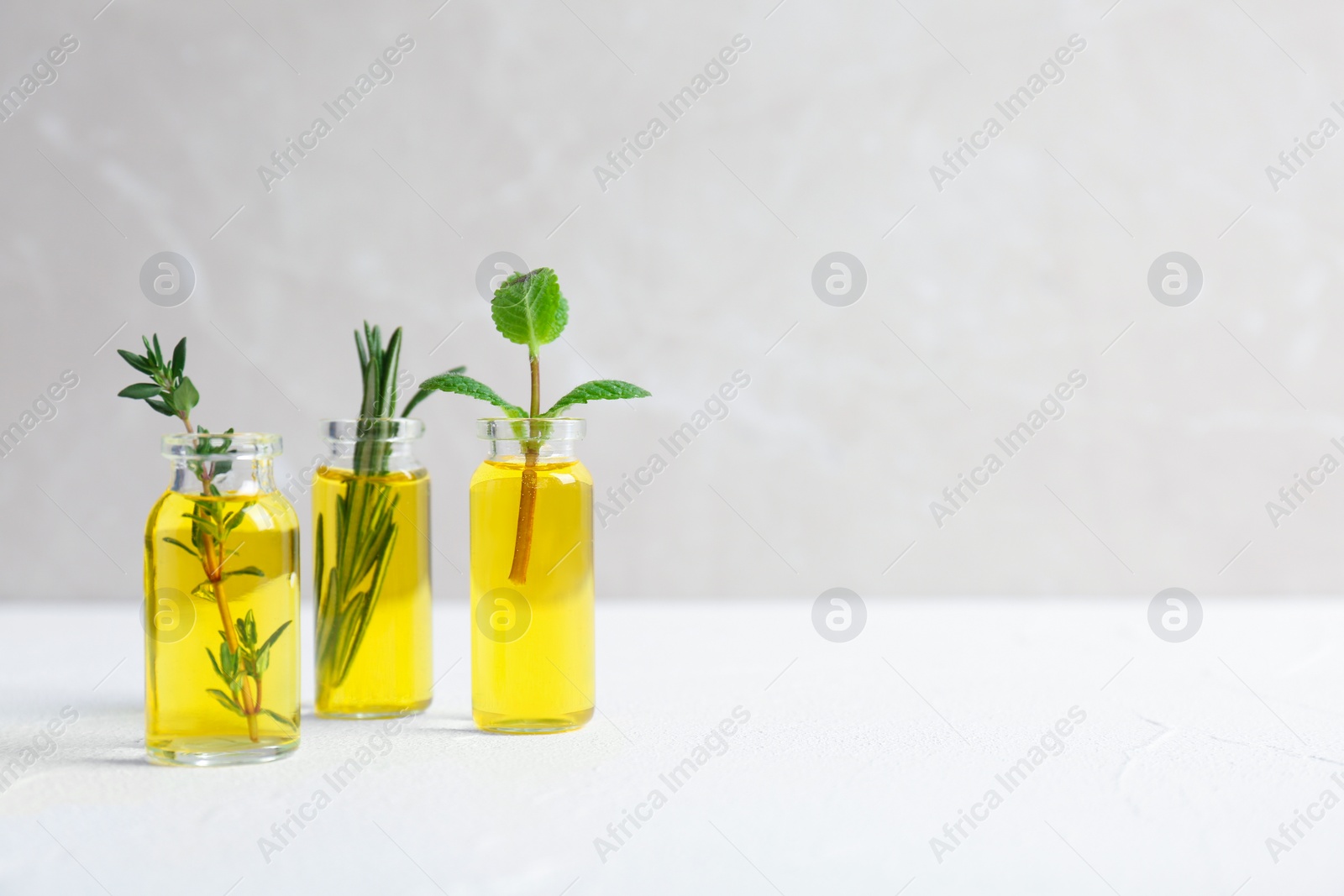 Photo of Bottles with essential oils and fresh herbs on light background