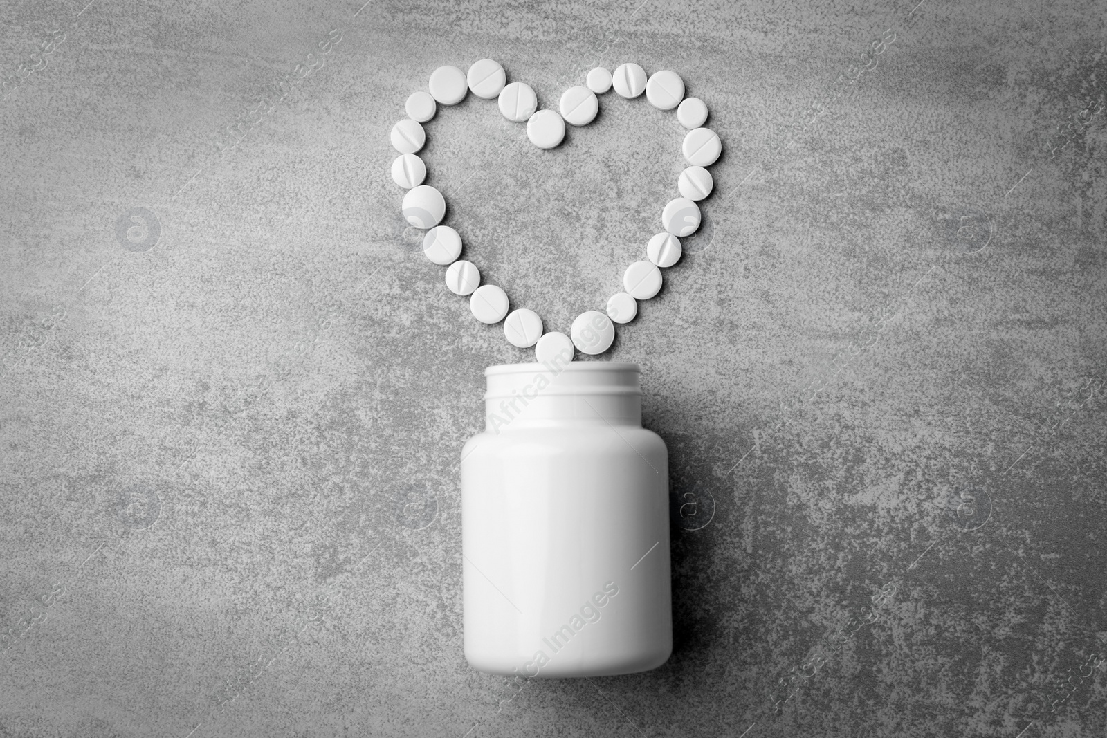 Photo of Bottle and heart of pills on grey background, flat lay