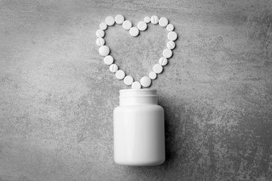 Bottle and heart of pills on grey background, flat lay