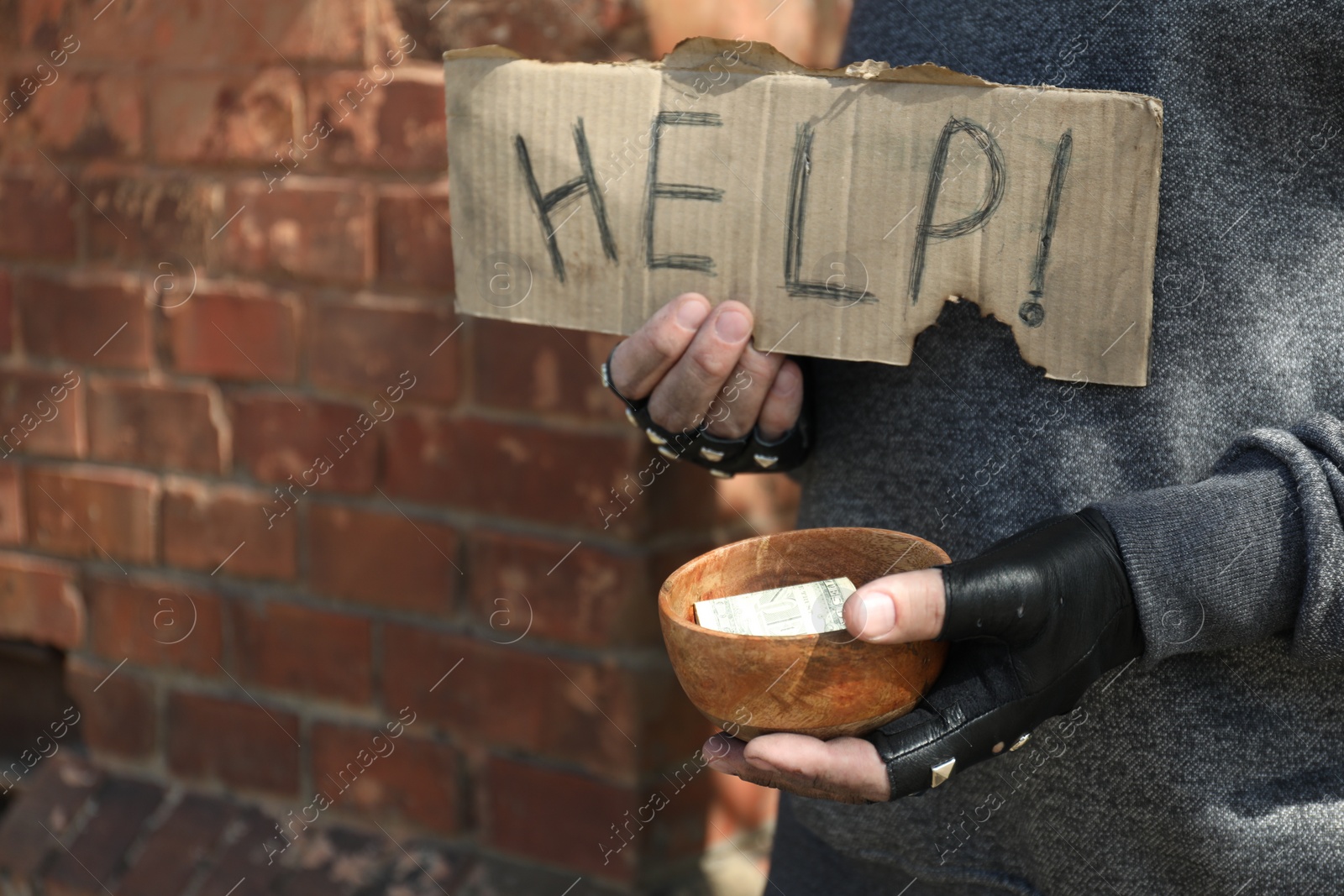 Photo of Poor homeless man holding help sign and bowl with donations outdoors, closeup. Space for text