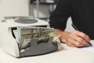 Photo of Modern banknote counter with money and blurred view of man working at white table indoors