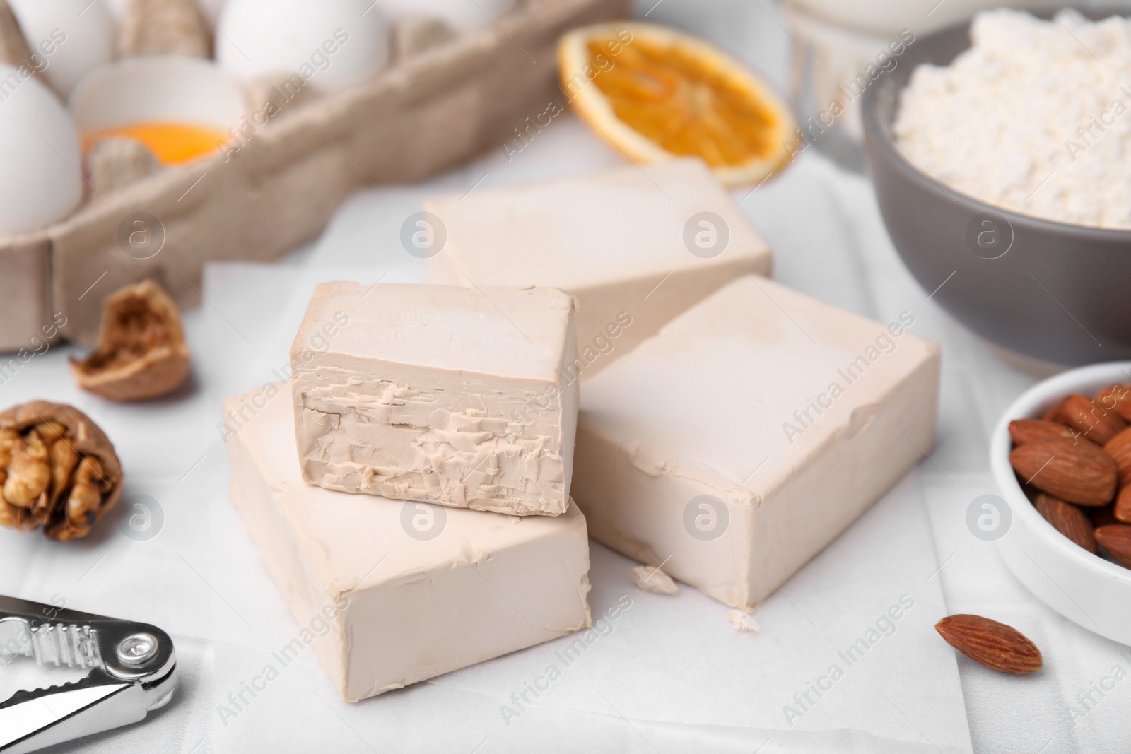 Photo of Blocks of compressed yeast and ingredients for dough on white table, closeup