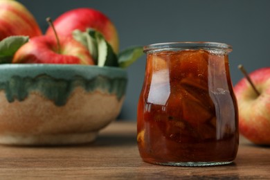 Tasty apple jam in glass jar and fresh fruits on wooden table, space for text