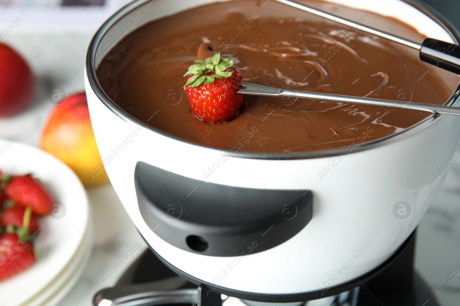 Photo of Dipping strawberry into pot with chocolate fondue on table, closeup